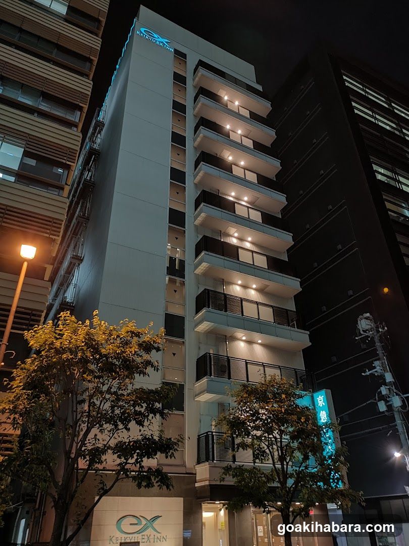 Night shot of a modern multi-story building with illuminated balconies and signage reading 'KEIKYU EX INN' at the base, surrounded by streetlights and trees.