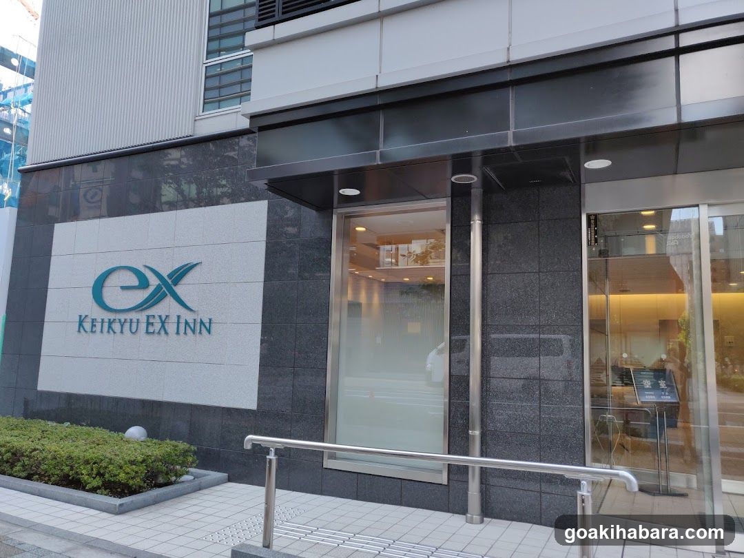Modern building entrance with glass doors and signage reading 'Keikyu EX Inn' on a light panel wall.