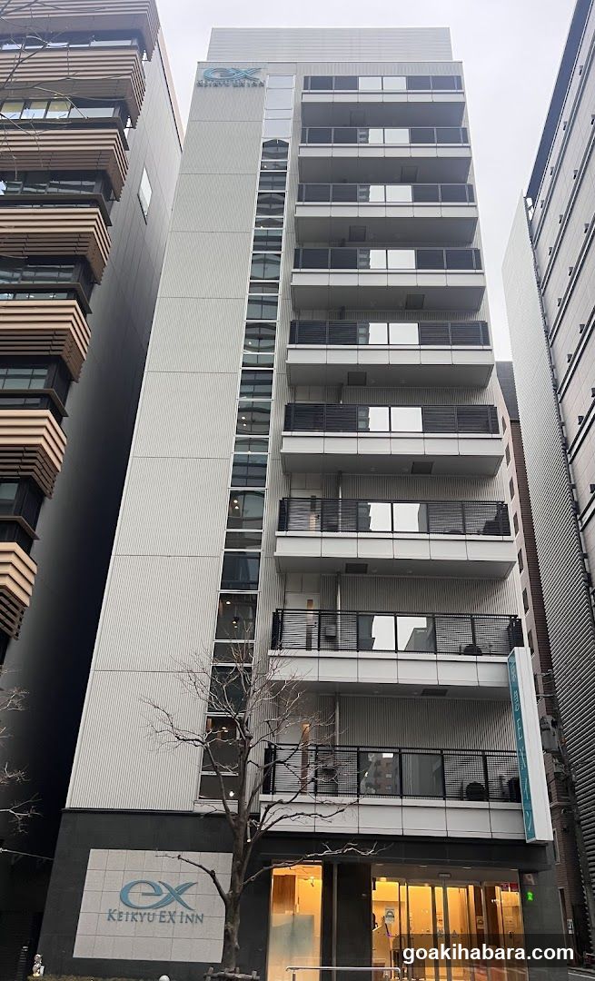 Modern multi-story building with balconies and glass entrance. Visible signage includes 'EX' logo and 'KEIKYU EX INN' on the lower facade. Entrance features illuminated glass doors.