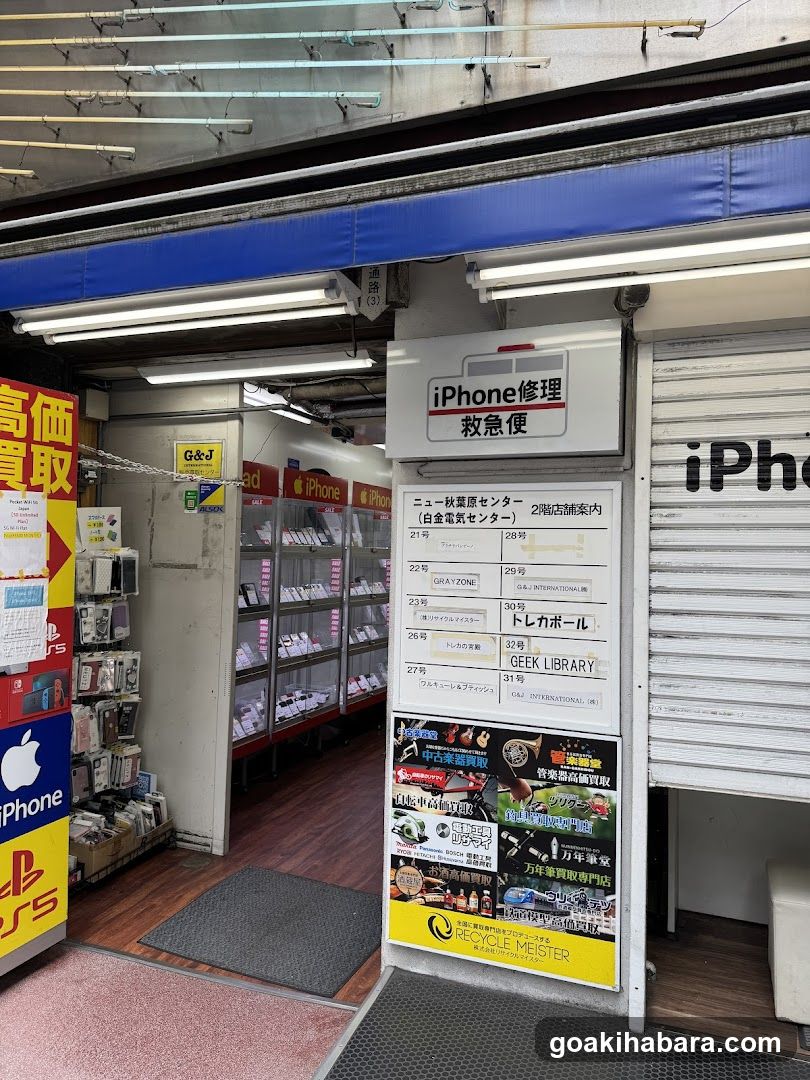 A storefront with visible signage including 'iPhone 修理 救急便' and various advertisements. The entrance leads to a shop interior displaying products on shelves.