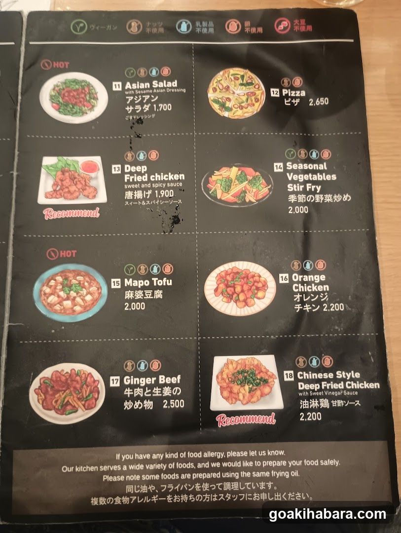 A black menu page featuring hot and recommended dishes with Japanese and English descriptions, prices in yen, and icons indicating dietary options.