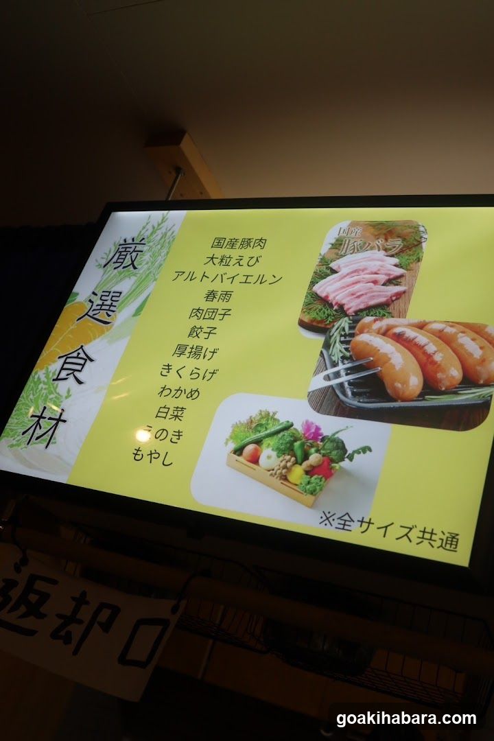 A menu board displaying sushi ingredients and items, including 'Kokoe Nikun', 'Otake Ebi', 'Alto Bairelun', 'Haruame', 'Nikunko', 'Atsukage', 'Kikurake', 'Baiyase', 'Koniki', and 'Moyashi'. The board also features images of sliced fish, sausages, and a vegetable box.