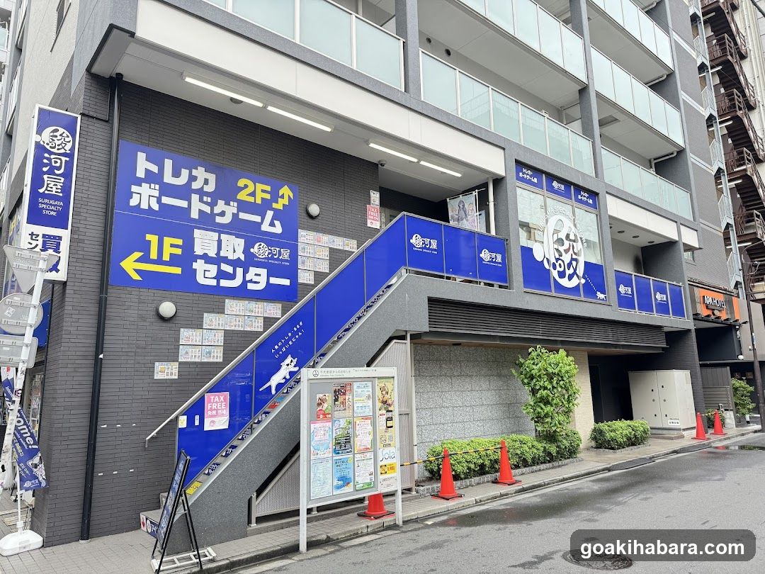 Exterior view of Kawashima Real Estate Agency (河屋) showing blue signage indicating 'Toreka 2F' and 'Purchase Center 1F'. A staircase leads up to the second floor, with property listings displayed on the wall. Orange traffic cones line the sidewalk.