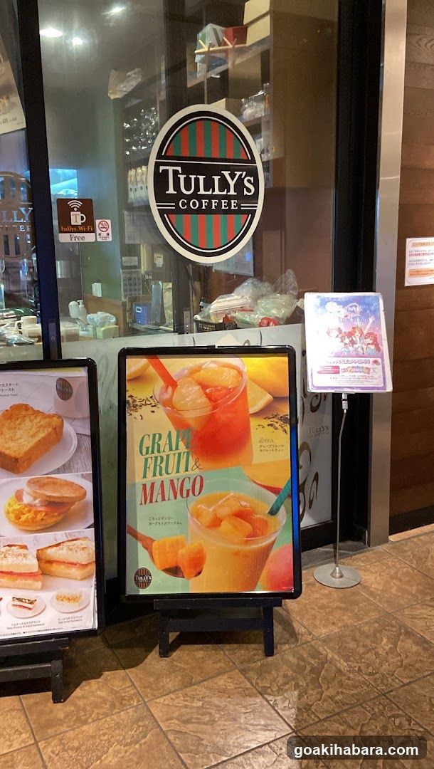 A storefront of Tully's Coffee with a visible logo on the glass door. Outside, there are two menu boards displaying food items and beverages.