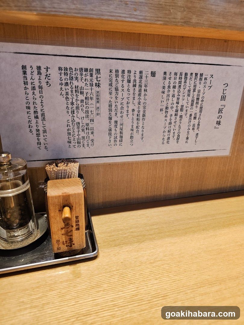 Close-up of a wooden counter in a Japanese restaurant featuring a metal tray with salt and pepper shakers, chopsticks in a holder, and a menu board describing various sushi dishes.