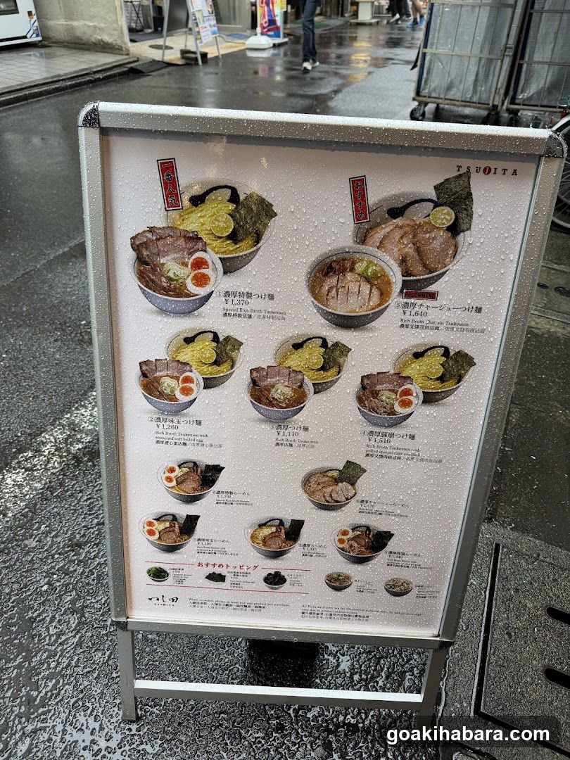 A standing menu board displaying various ramen dishes with prices in yen, featuring images of bowls and ingredients like pork, seaweed, and eggs.