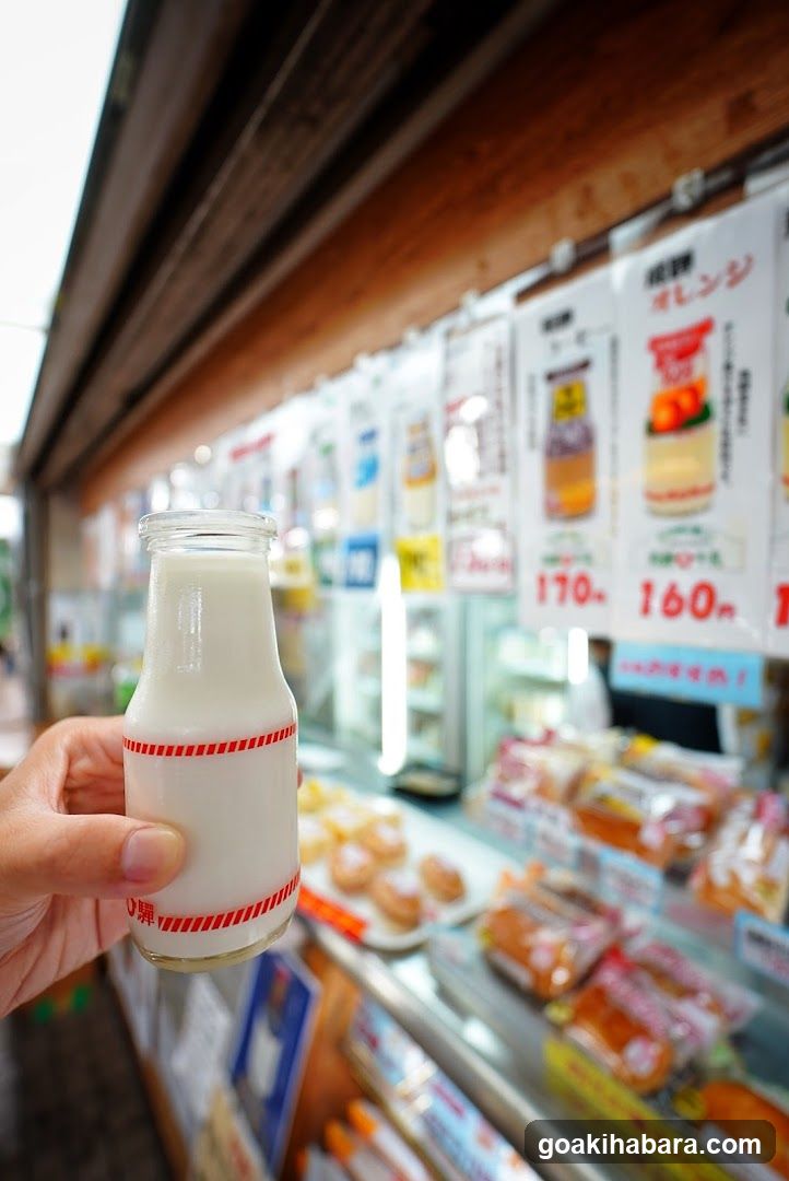 Hand holding milk bottle in front of shop display