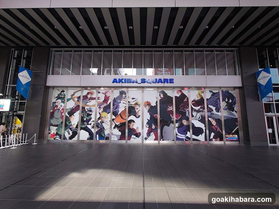Photo of the physical exterior entrance storefront facade with visible signage reading 'AKIBA SQUARE' above glass doors featuring anime character murals.