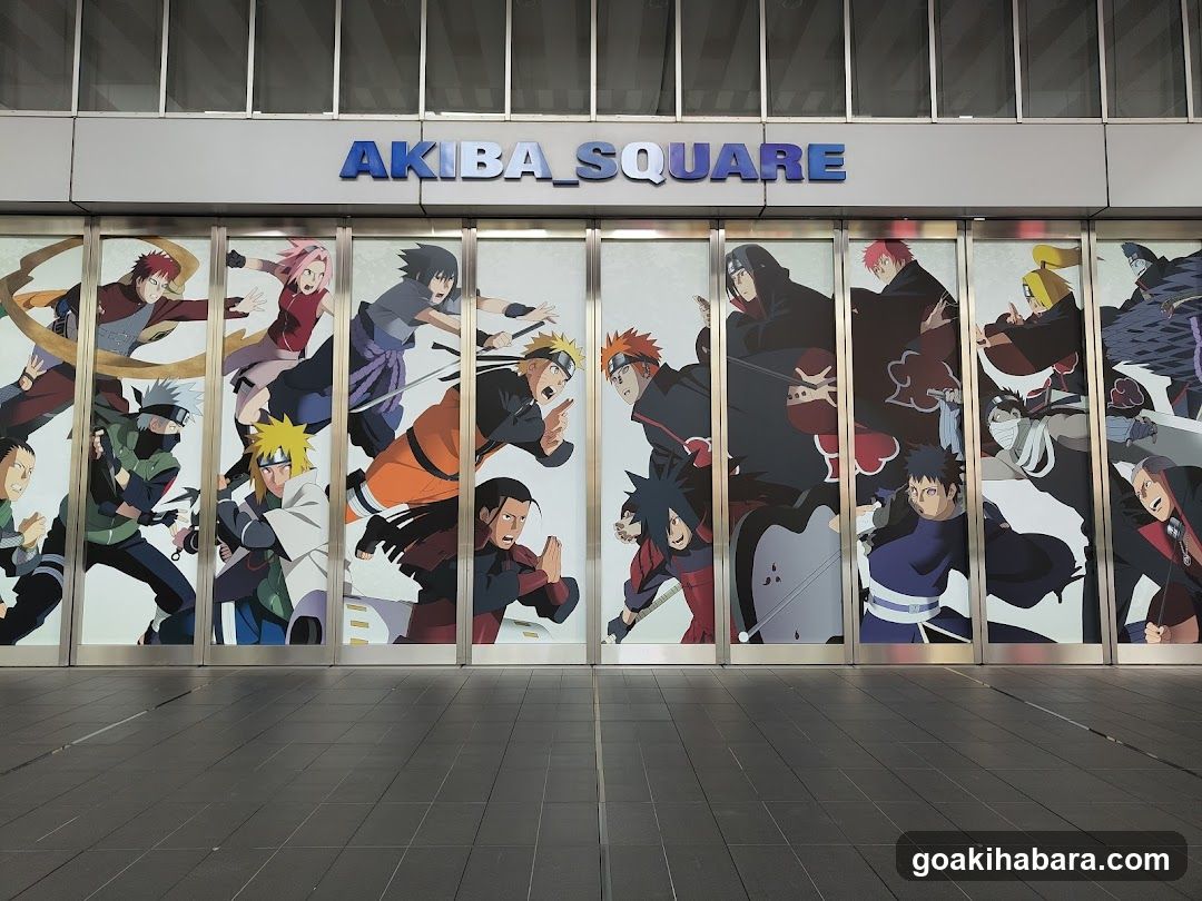 Photo of the physical exterior entrance to Akiba Square, featuring a large glass facade with anime character murals and blue signage reading 'AKIBA SQUARE' above.