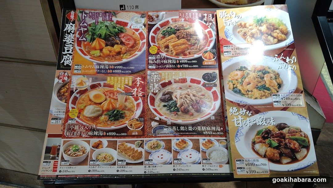 A menu board featuring various Japanese dishes, including ramen bowls with different toppings like pork, egg, and vegetables. The menu includes prices in yen and showcases a variety of noodle soups and side dishes.