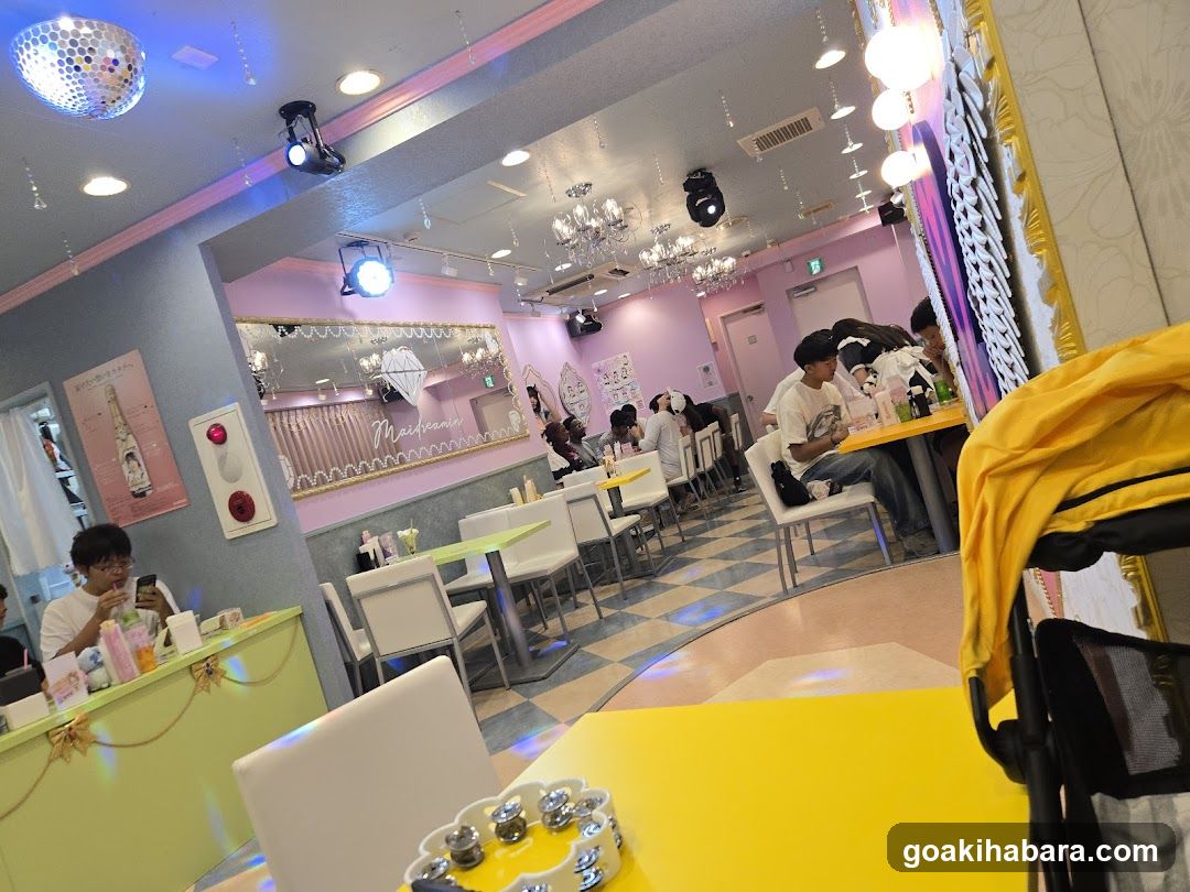 Interior of a brightly lit cafe or restaurant with pink and yellow decor, chandeliers, disco ball lighting, and customers seated at tables.