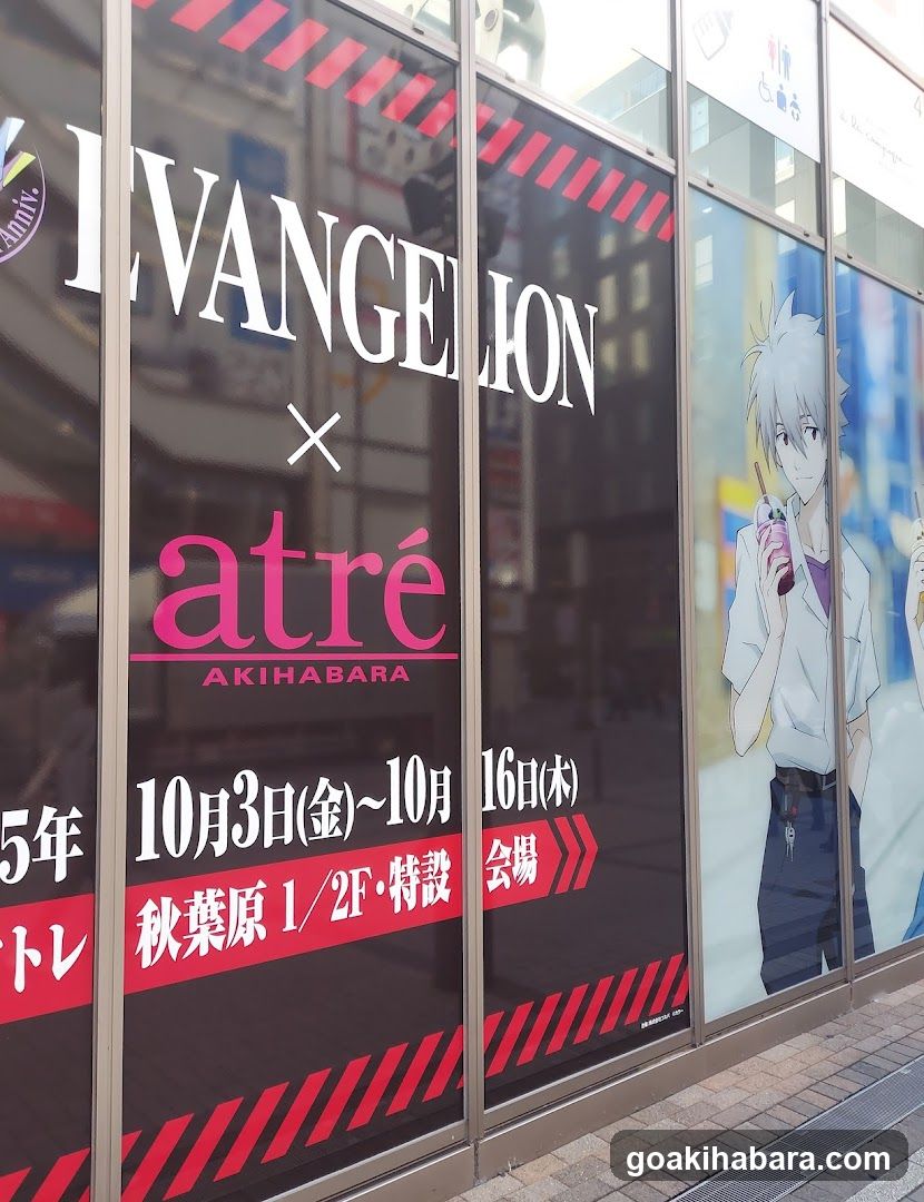 A storefront window display featuring a collaboration between Evangelion and atré Akihabara. The glass facade shows large white lettering spelling 'EVANGELION' with a pink 'atré' logo below it. Dates of October 3rd to October 16th are listed, along with location details indicating the event is at atré Akihabara on the first or second floor. An anime character illustration appears on the right side of the window.
