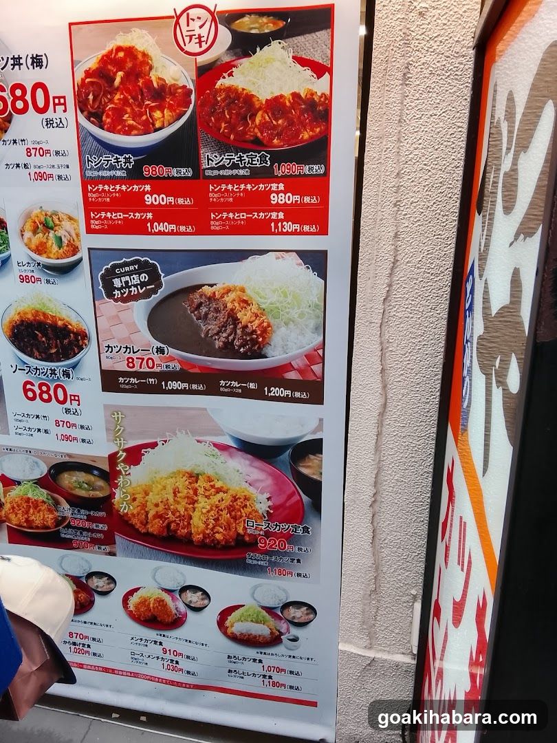 A vertical menu board displaying various Japanese dishes with prices and images, including curry rice, tonkatsu, and other fried items.