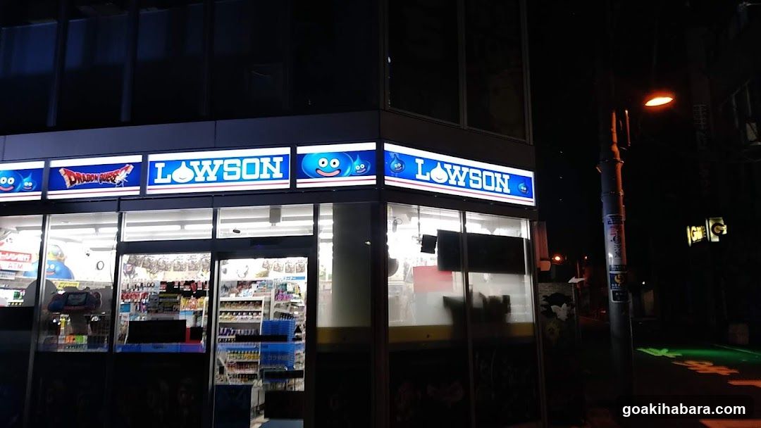 A brightly lit Lowson convenience store storefront at night, featuring illuminated signage with the brand name and mascot logo above glass windows displaying shelves of products inside.