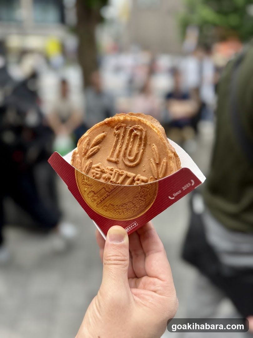 Hand holding a golden-brown waffle cookie with '10' embossed on it, in a red paper wrapper.