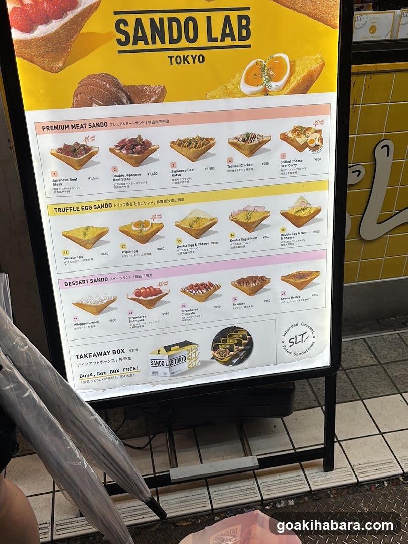 A vertical menu board displaying various sandwich options from Sando Lab in Tokyo, categorized into Premium Meat Sando, Truffle Egg Sando, Dessert Sando, and Takeaway Box.