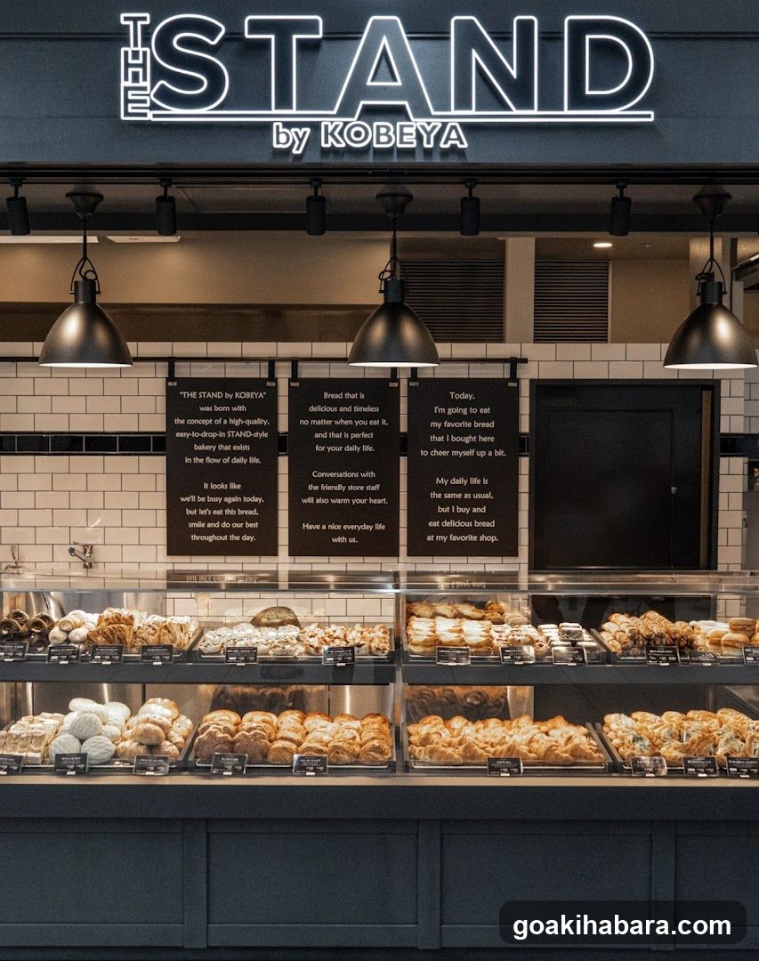 Storefront of The Stand by KobeYa featuring illuminated signage, hanging pendant lights, and a display case filled with various breads and pastries.