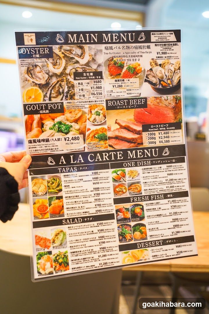 A hand holds a printed menu featuring sections like 'MAIN MENU' with items such as Oysters, Gout Pot, and Roast Beef; 'A LA CARTE MENU' listing Tapas, One Dish, Salad, Fresh Fish, and Dessert options.