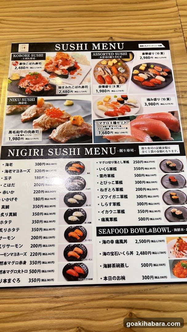 A printed sushi menu displayed on a wooden table, featuring sections for Kobore Sushi, Assorted Sushi, Niku Sushi, and Nigiri Sushi with prices in JPY.
