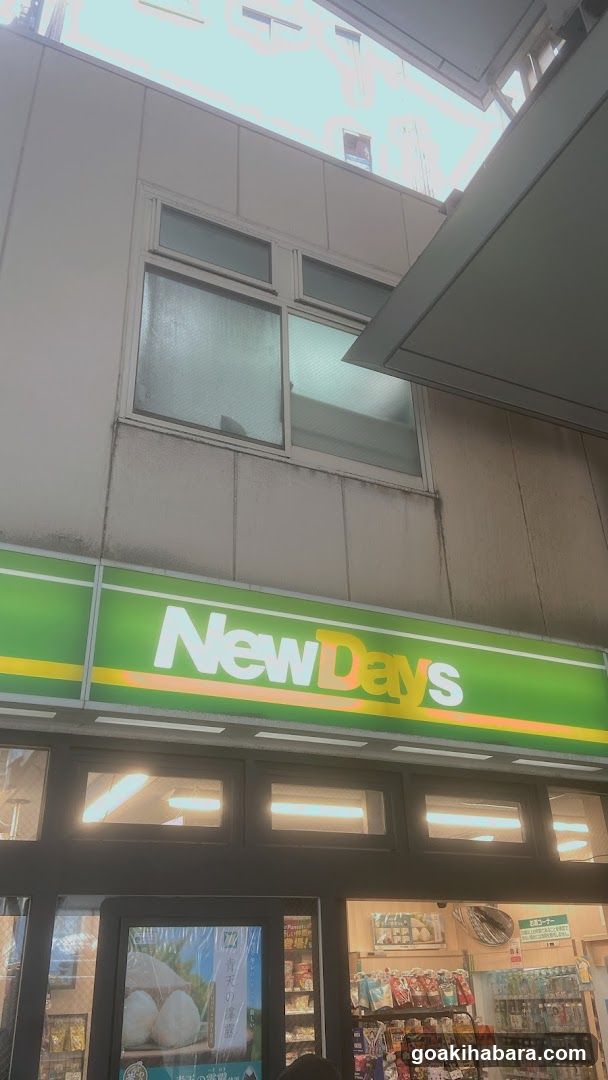 Photo of the physical exterior entrance and storefront facade of a NewDays convenience store, showing the green and yellow signage with 'NewDays' logo above glass doors and windows.