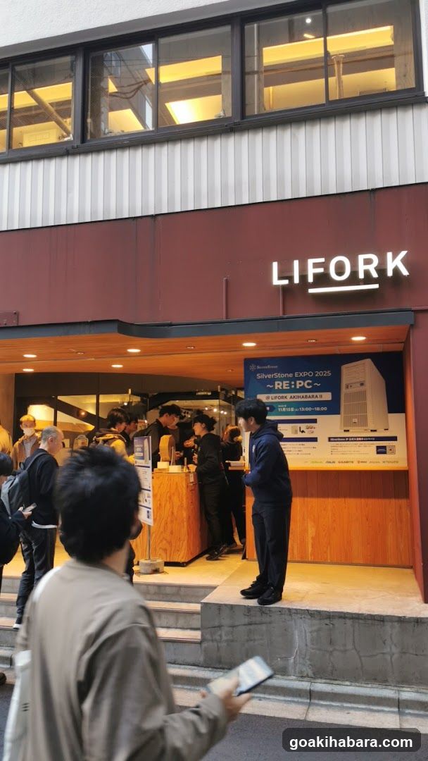 Photo of the exterior storefront facade featuring a prominent 'LIFORK' sign above an open entrance. A group of people are gathered near wooden counters inside, while one person stands outside looking at a phone. A promotional poster for 'SilverStone EXPO 2025' is visible on the right side.